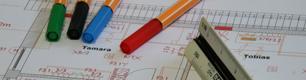 Ausschnitt aus einem ausgedruckten Grundrissplan mit Elektroplanung. Auf dem Ausdruck liegen bunte Stifte und ein Lineal.